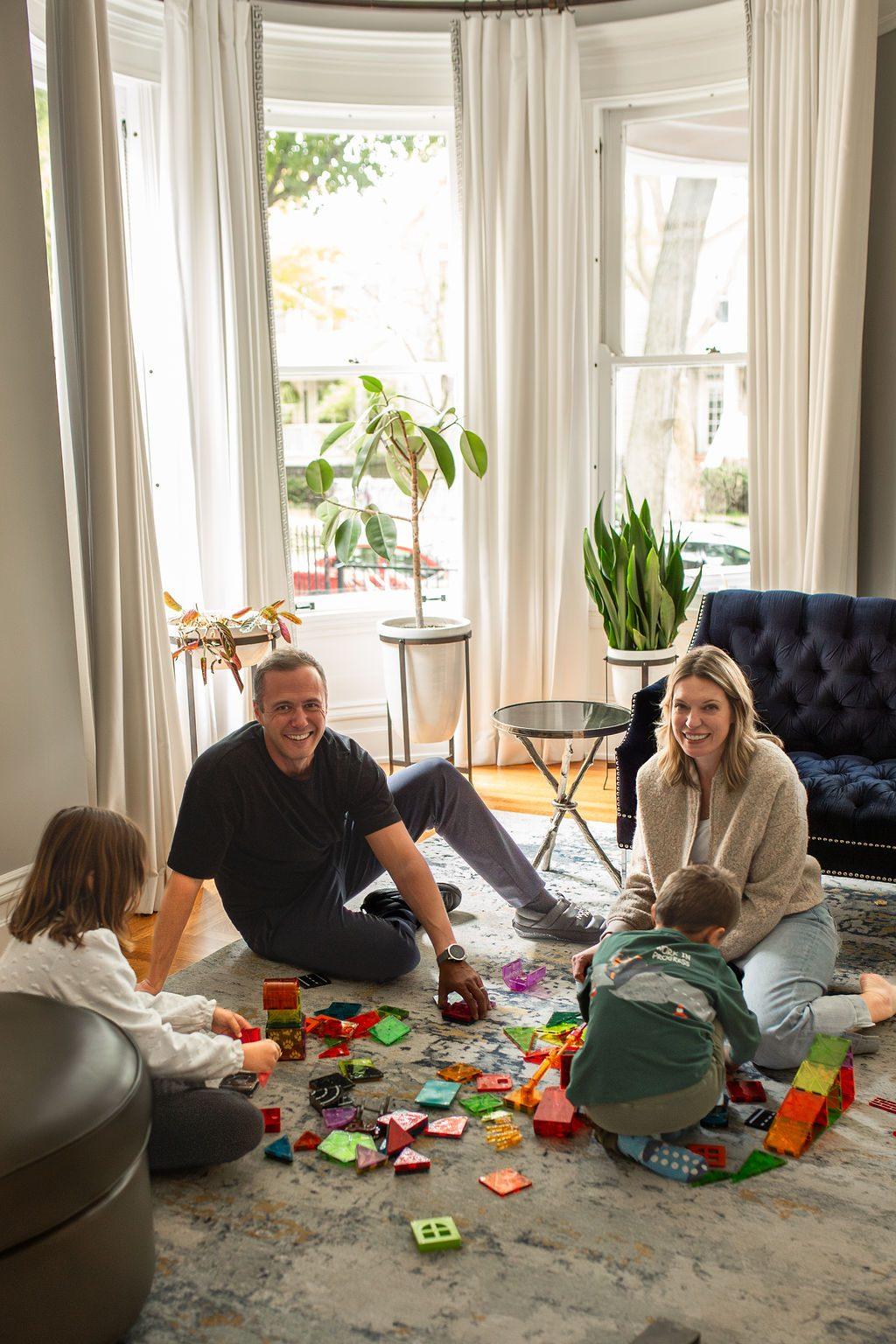 A family plays together on the floor with colorful building blocks in a bright room