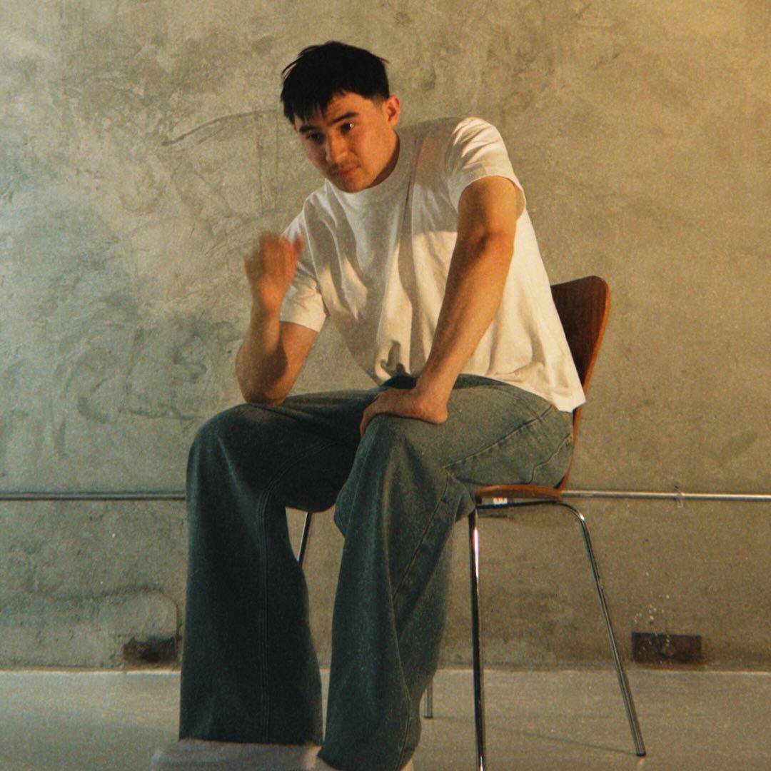 Person in a white t-shirt and jeans sitting on a chair against a textured wall