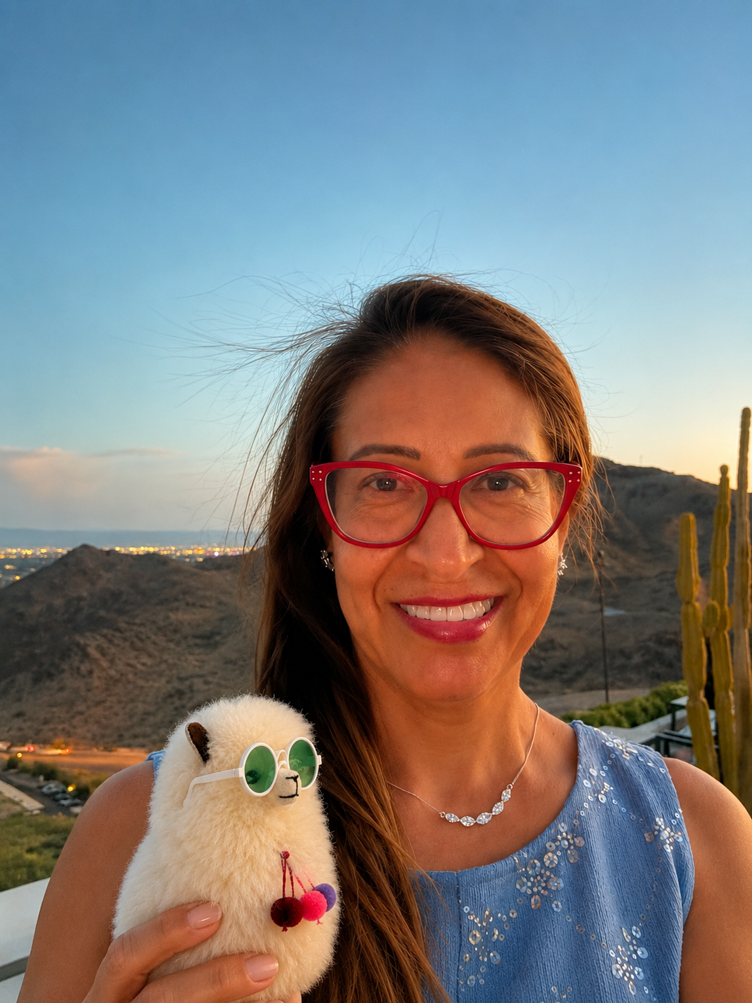 Woman with red glasses smiles, holding a stuffed toy against a scenic background