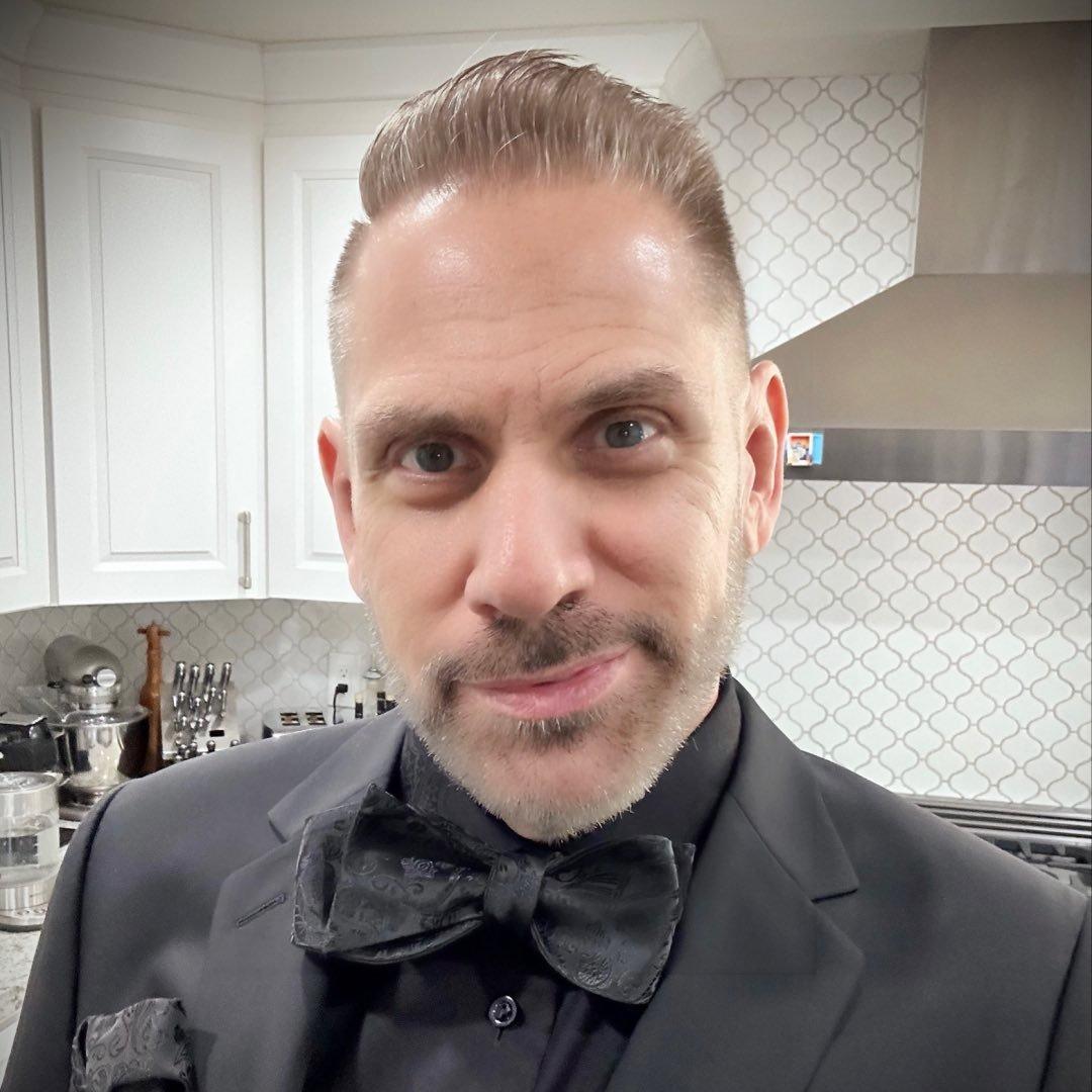 Man in formal attire with a bow tie, standing in a modern kitchen
