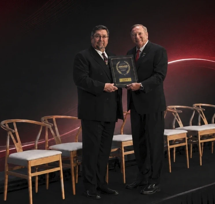Two men in formal attire holding an award plaque on stage