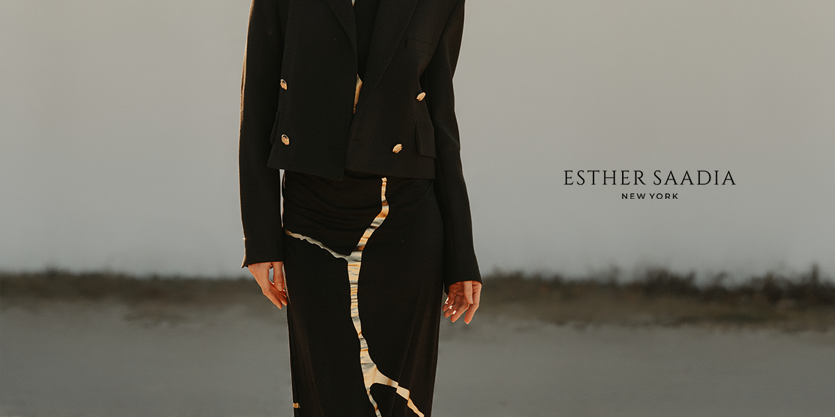 Model wearing a black tailored jacket and flowing skirt with metallic detailing, photographed outdoors for Esther Saadia New York.
