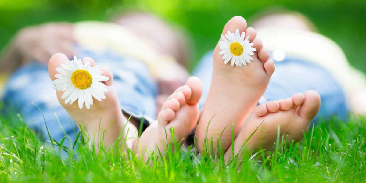 Close-up of feet with daisies between toes, lying on grass.
